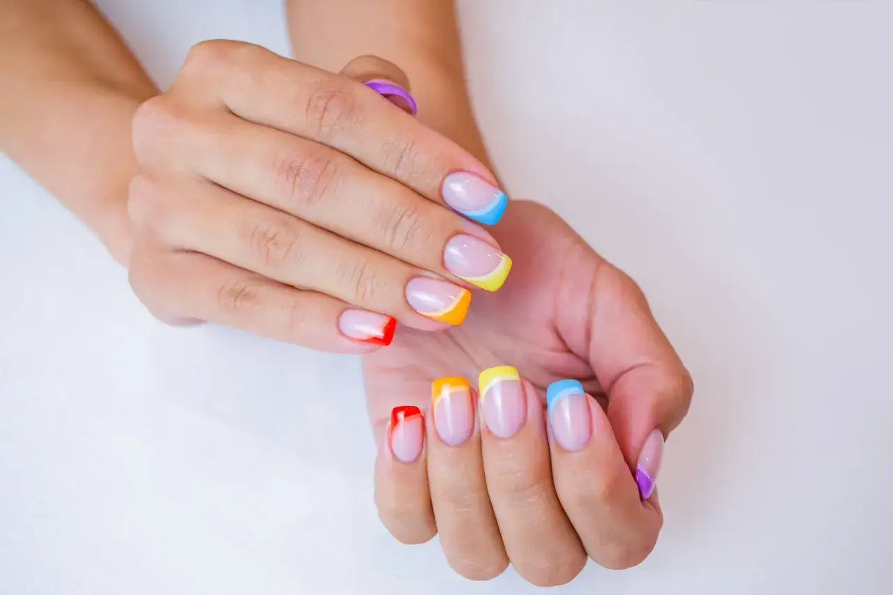 Dłonie z kolorowym francuskim manicure w odcieniach tęczy.