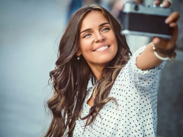 Uśmiechnięta brunetka robi sobie selfie starą kamerą.